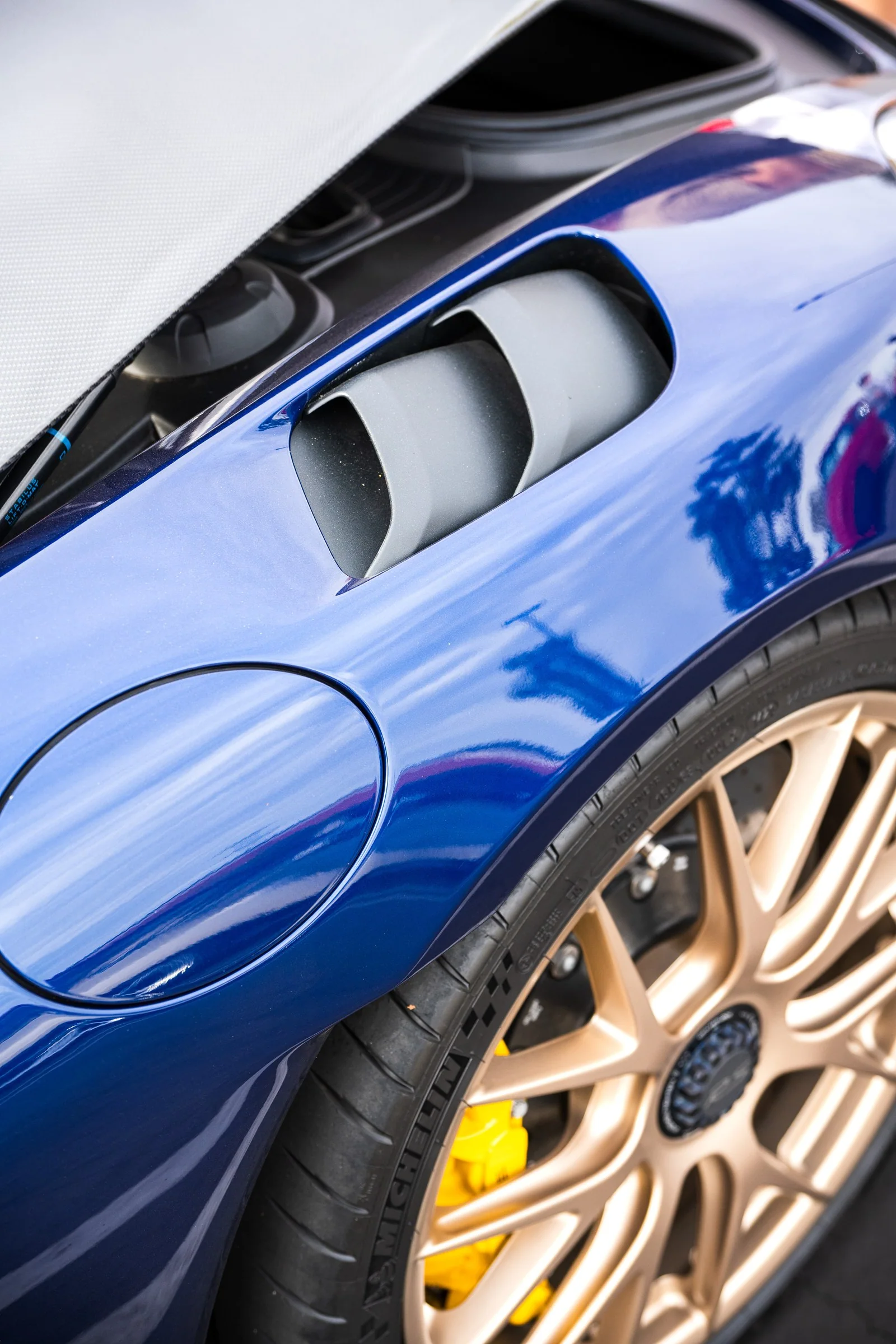 Vented blue Porsche Cayman fender above a bronze wheel.